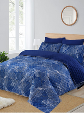 Blue floral-patterned comforter set on a bed in a bright bedroom.